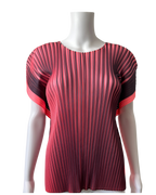 A short-sleeve pleated top displayed on a white mannequin torso. The top features a vertical pleated design with a color gradient transitioning from pink on the sides to a vibrant aubergine 