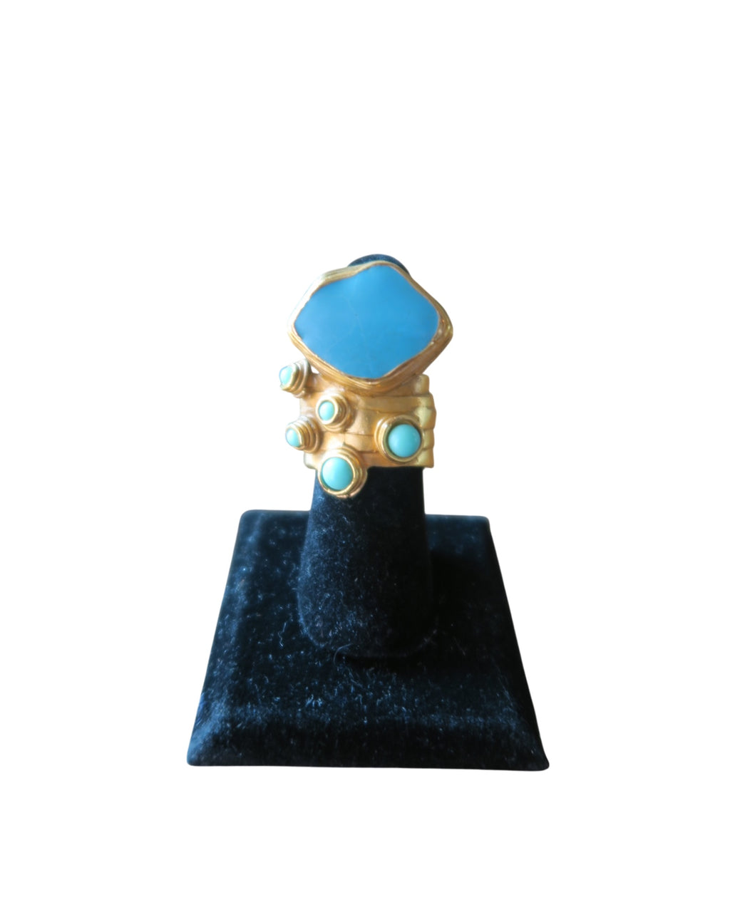 A gold ring with a large light blue hexagonal stone and smaller matching blue stones, displayed on a black velvet ring stand against a white background.
