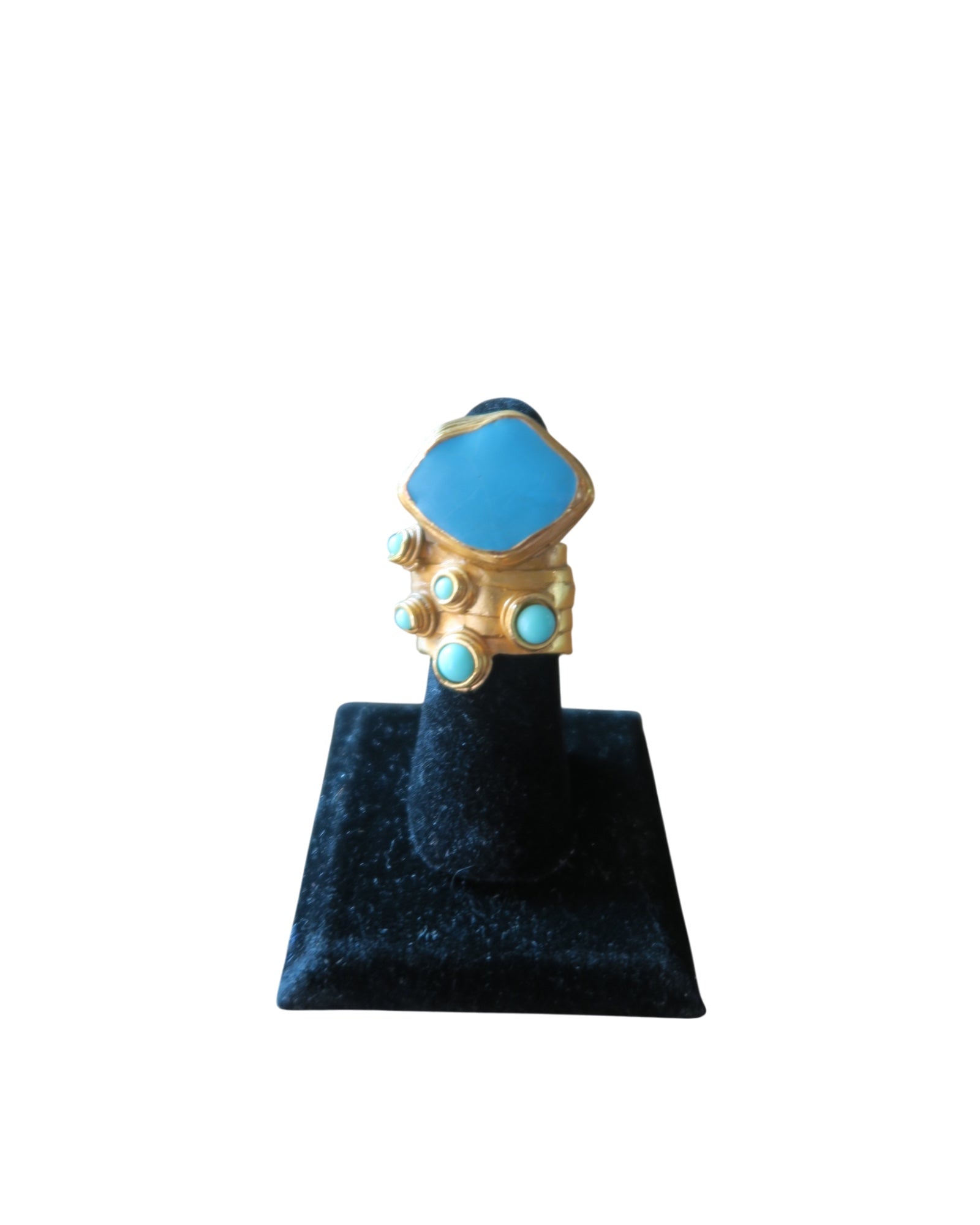 A gold ring with a large light blue hexagonal center stone and four smaller matching blue stones, displayed on a black velvet ring stand against a white background.