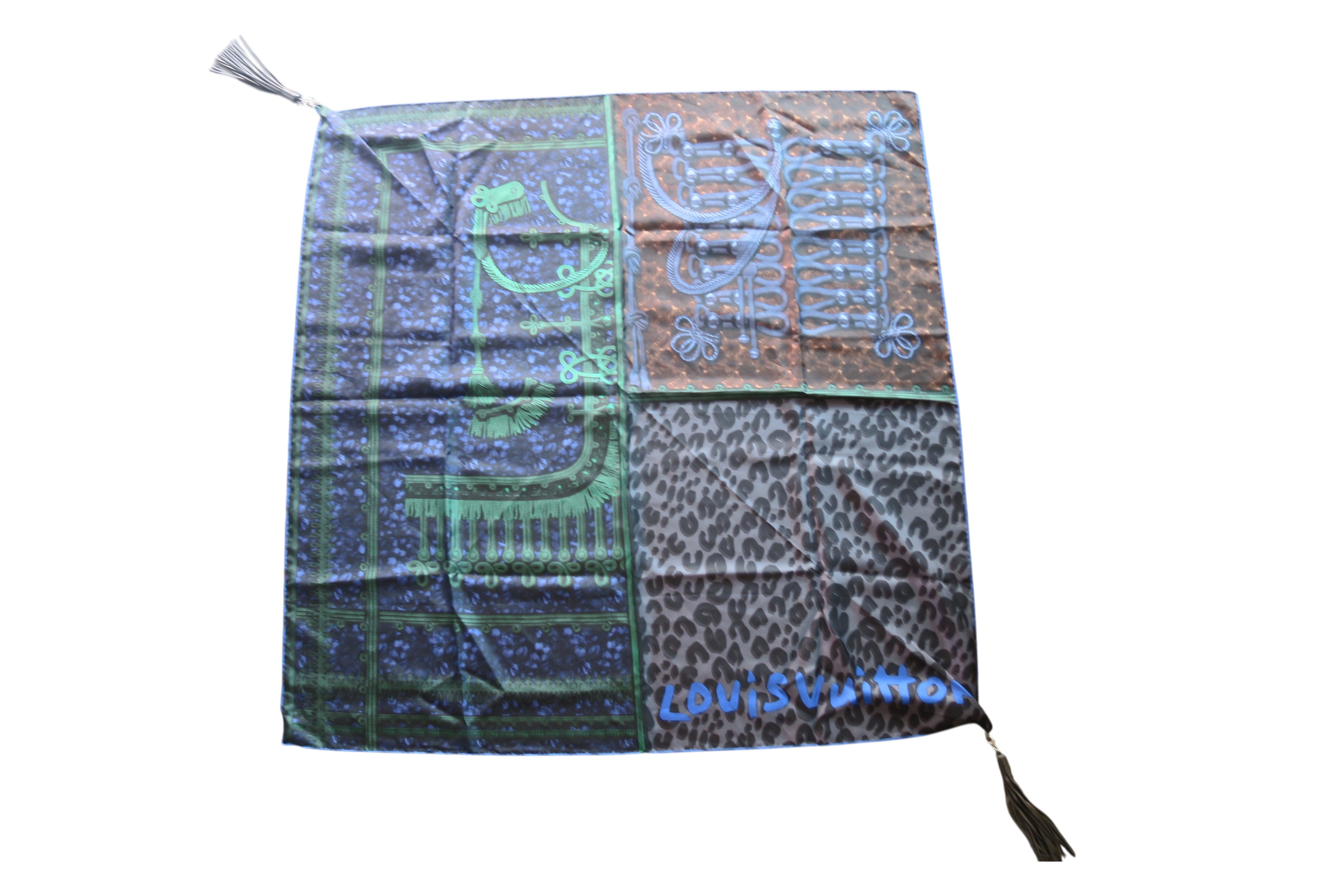 A square Louis Vuitton scarf featuring a four-quadrant print design with a green floral motif, a brown and blue script pattern, a leopard print, and a blue Louis Vuitton logo, complete with two white tassels.